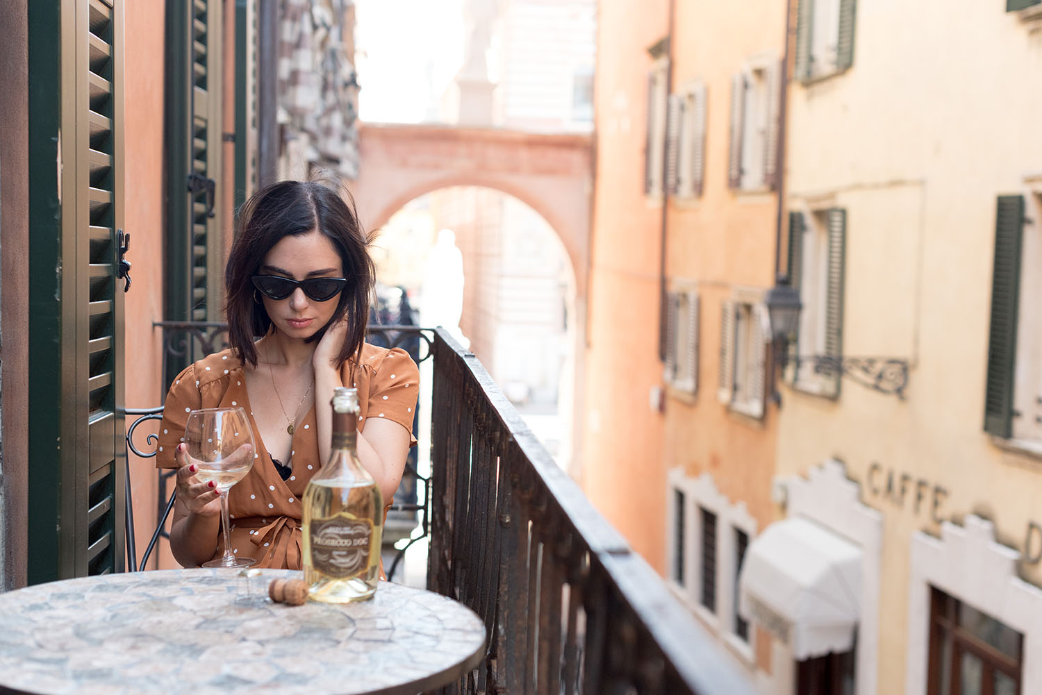 Top Canadian fashion blogger Cee Fardoe of Coco & Vera sits on a balcony in Verona, Italy, wearing a Sezane dress and Zara sunglasses