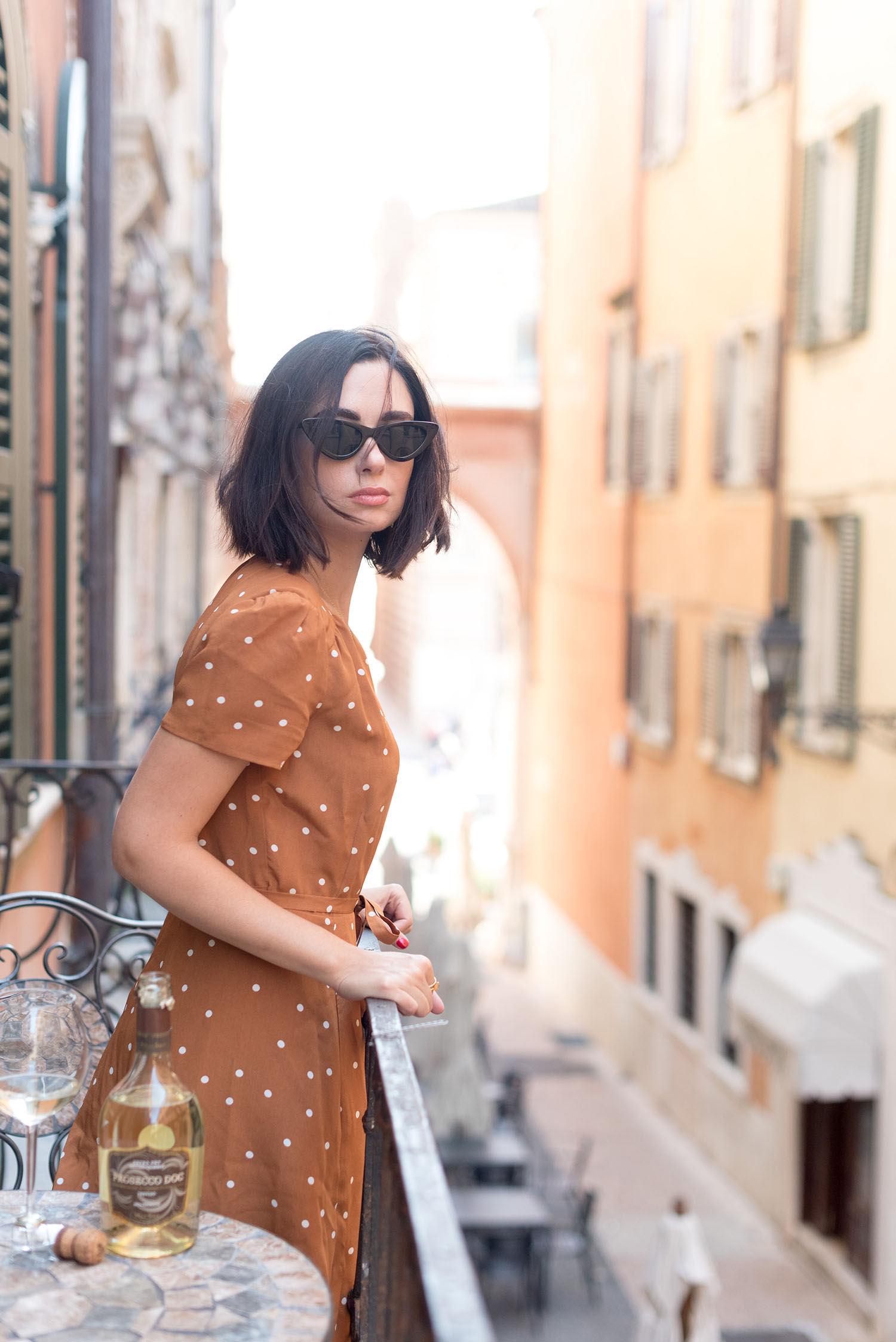 Top Winnipeg fashion blogger Cee Fardoe of Coco & Vera stands on a balcony in Verona, Italy, wearing a Sezane polkadot dress and Zara cat eye sunglasses