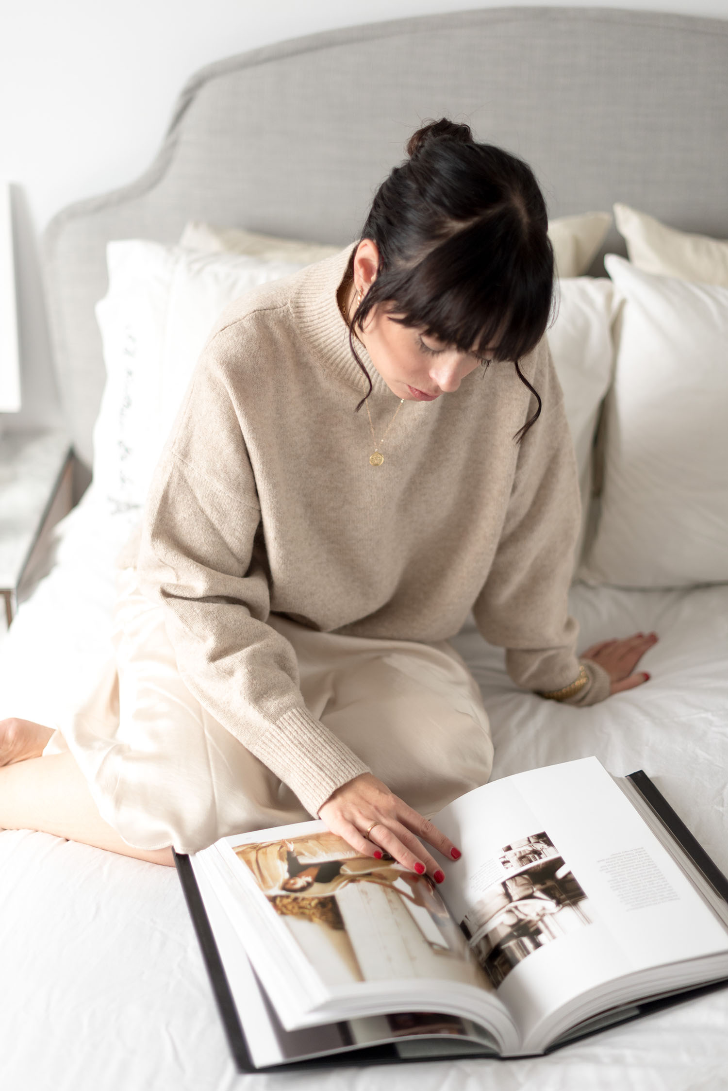 Top Winnipeg fashion blogger Cee Fardoe of Coco & Vera sits on her bed wearing a beige Pixie Market skirt and reading a Vogue book