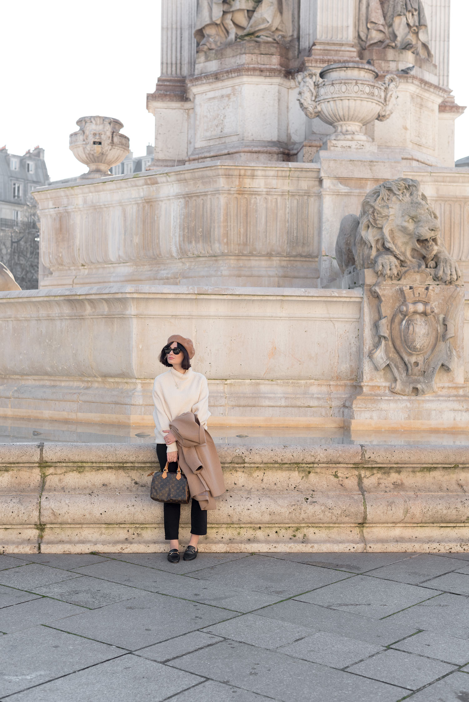 Top Canadian fashion blogger Cee Fardoe of Coco & Vera sits at Place Saint-Sulpice in Paris wearing a Glam Sesh Neil sweater and Mavi crop flared jeans