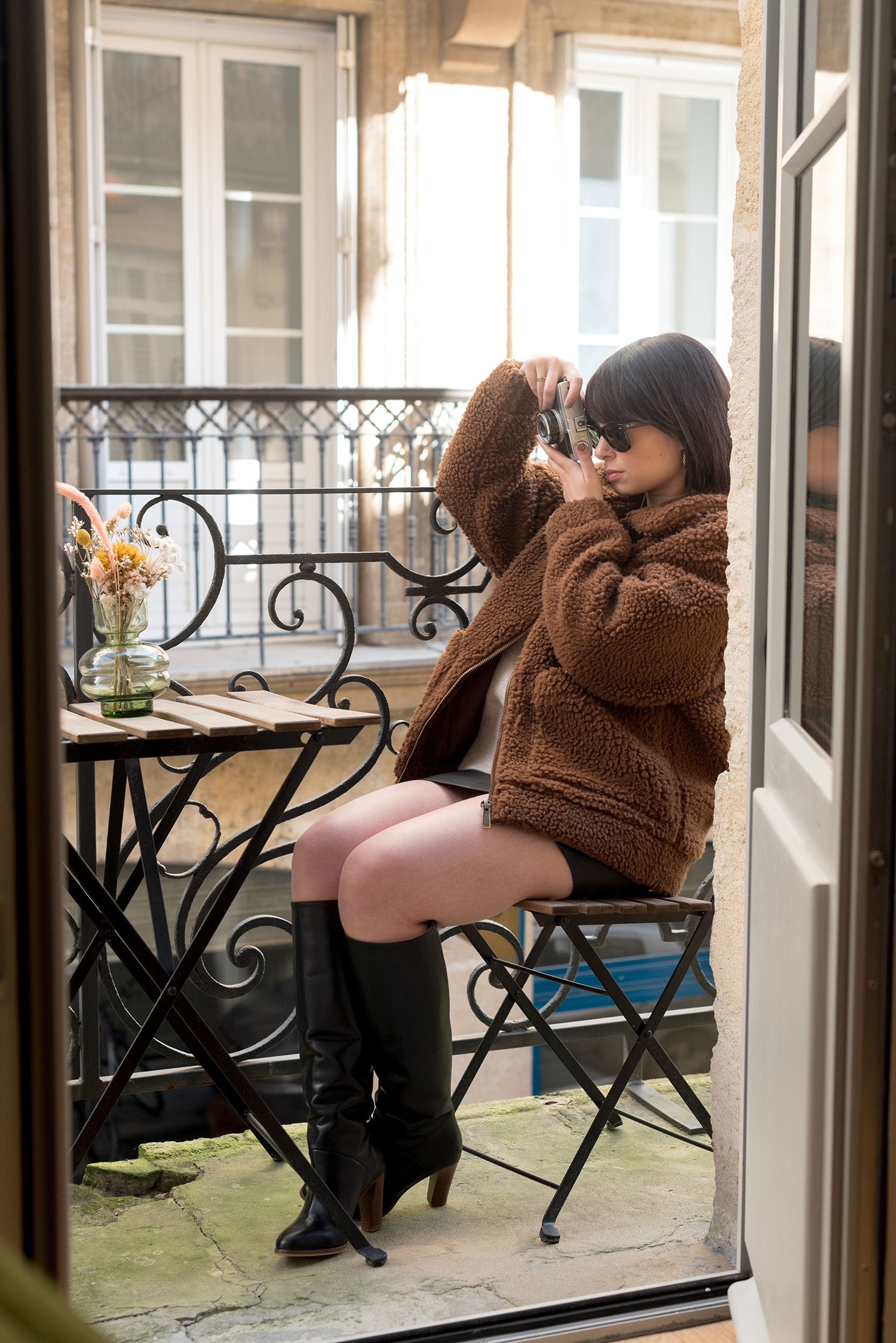 Top Canadian fashion blogger Cee Fardoe of Coco & Vera sits on the balcony at La Maison Fernand in Bordeaux wearing Suzanne Abby boots and a Garage Clothing teddy coat