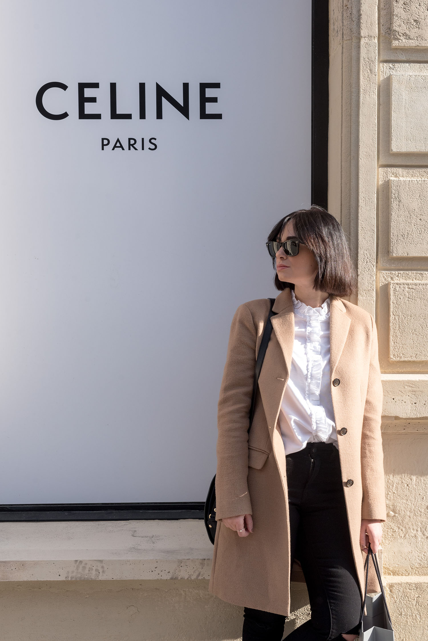 Portrait of top Canadian fashion blogger Cee Fardoe of Coco & Vera outside the celine store in Paris, wearing a Uniqlo camel coat and carrying an APC half-moon bag