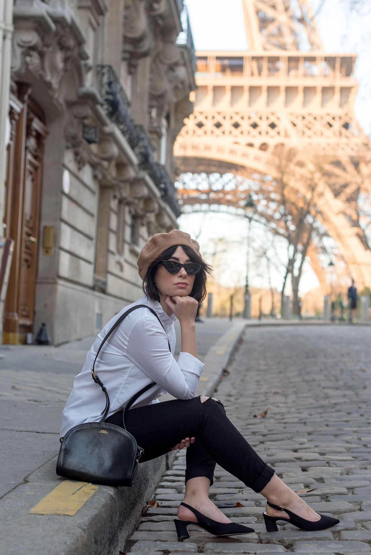 Top Canadian fashion blogger Cee Fardoe of Coco & Vera sits on a Parisian street near the Eiffel Tower wearing Mavi jeans and carrying an APC handbag