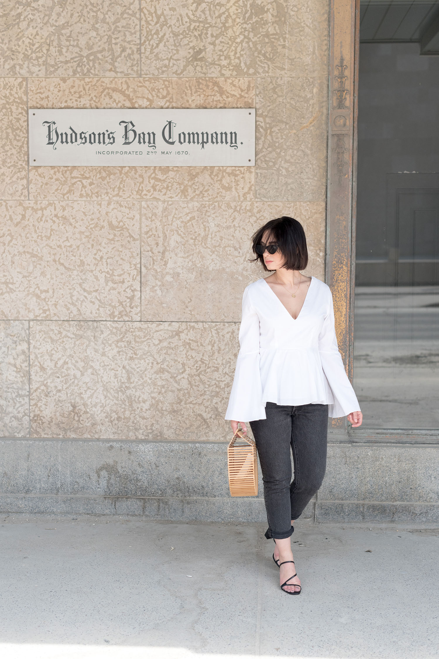 Top Canadian fashion blogger Cee Fardoe of Coco & Vera walks outside the Bay Downtown in Winnipeg wearing Zara sandals and carrying a bamboo cage bag, the wind blowing through her hair