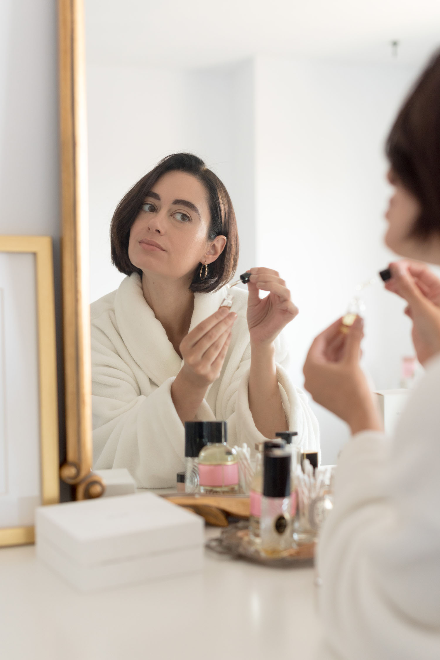 Top Winnipeg beauty blogger Cee Fardoe of Coco & Vera applies Bastide Elixir II oil while looking in a mirror