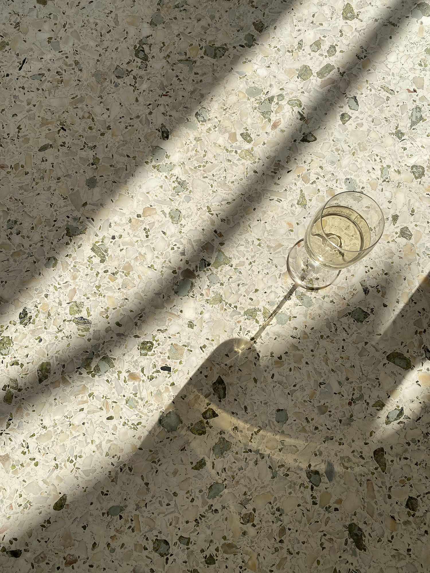 Coco & Vera - Glass of white wine in the sunlight on a terrazzo marble floor in greece