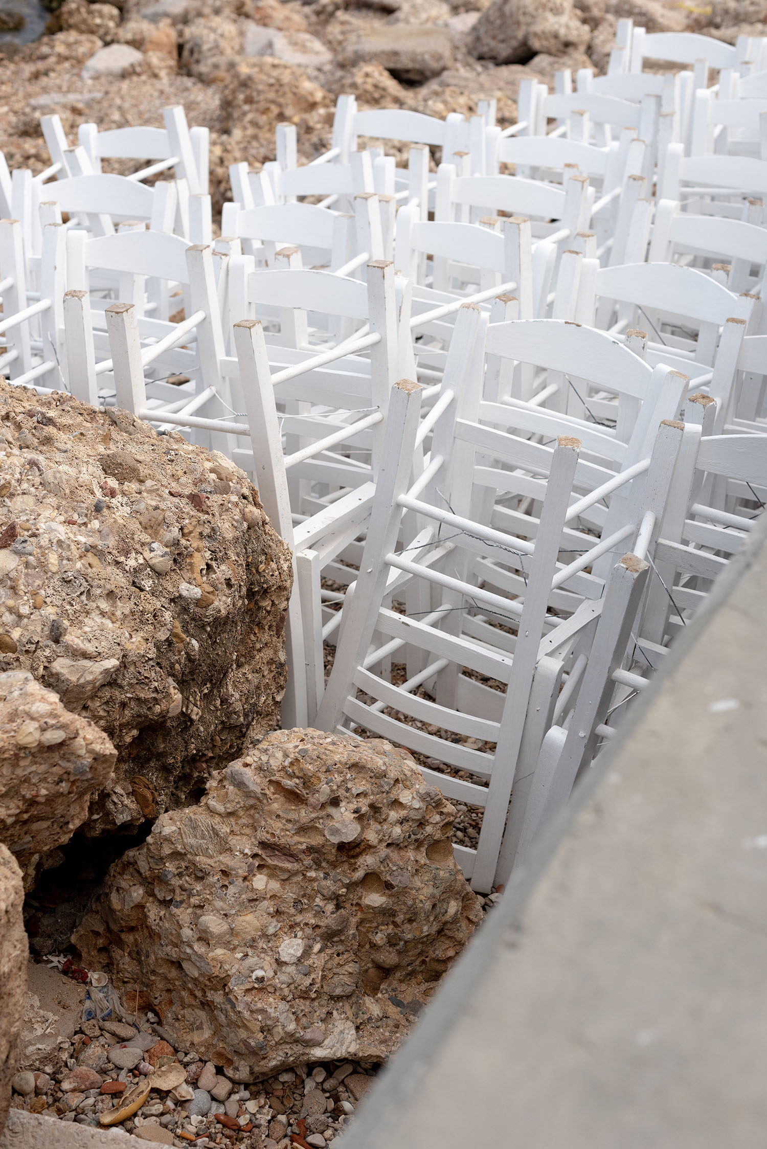 Coco & Vera - White restaurant chairs stacked on a rocky beach on Spetses Island in Greece