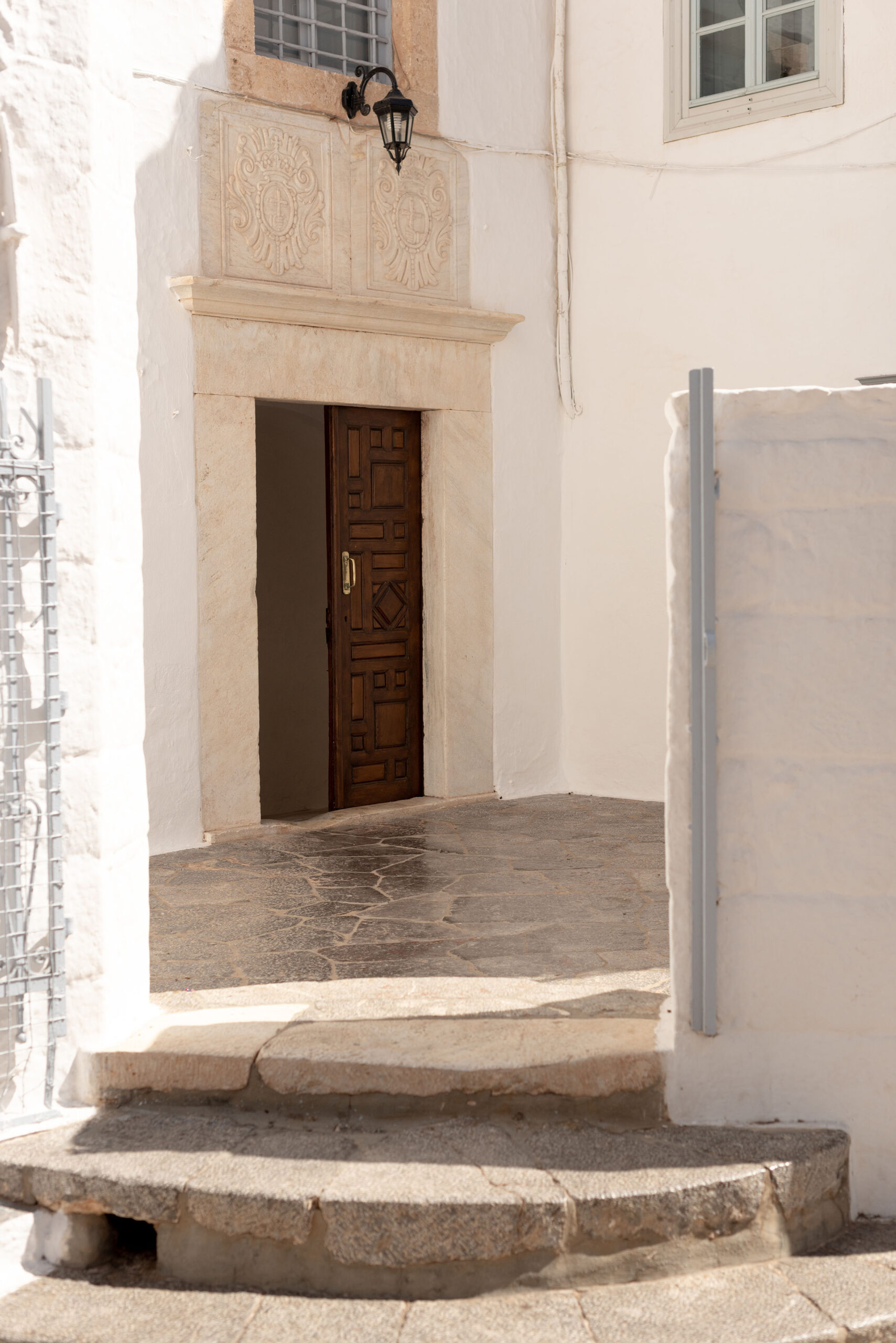 Coco & Vera - A brown wooden door inside a stone courtyard in Hydra Town in Greece